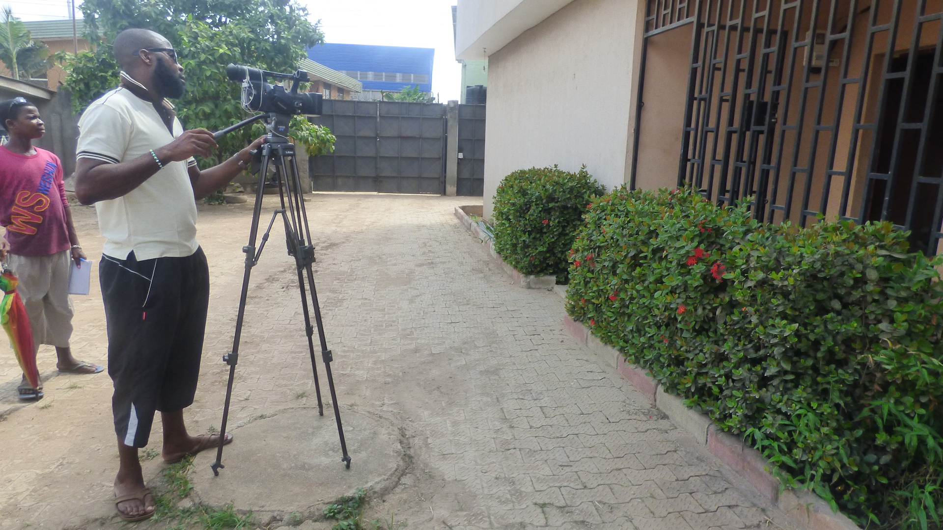 Kunle Odunewu filming on location with a video camera on a tripod